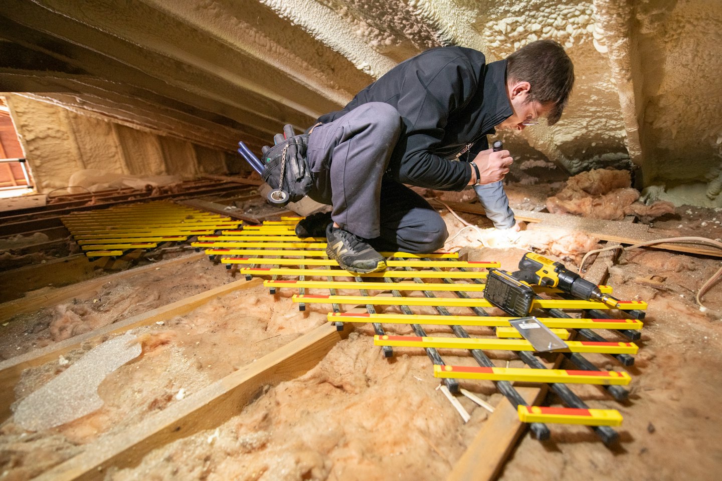 Clima LLC technician working on a sealed attic floor with insulation and a drill