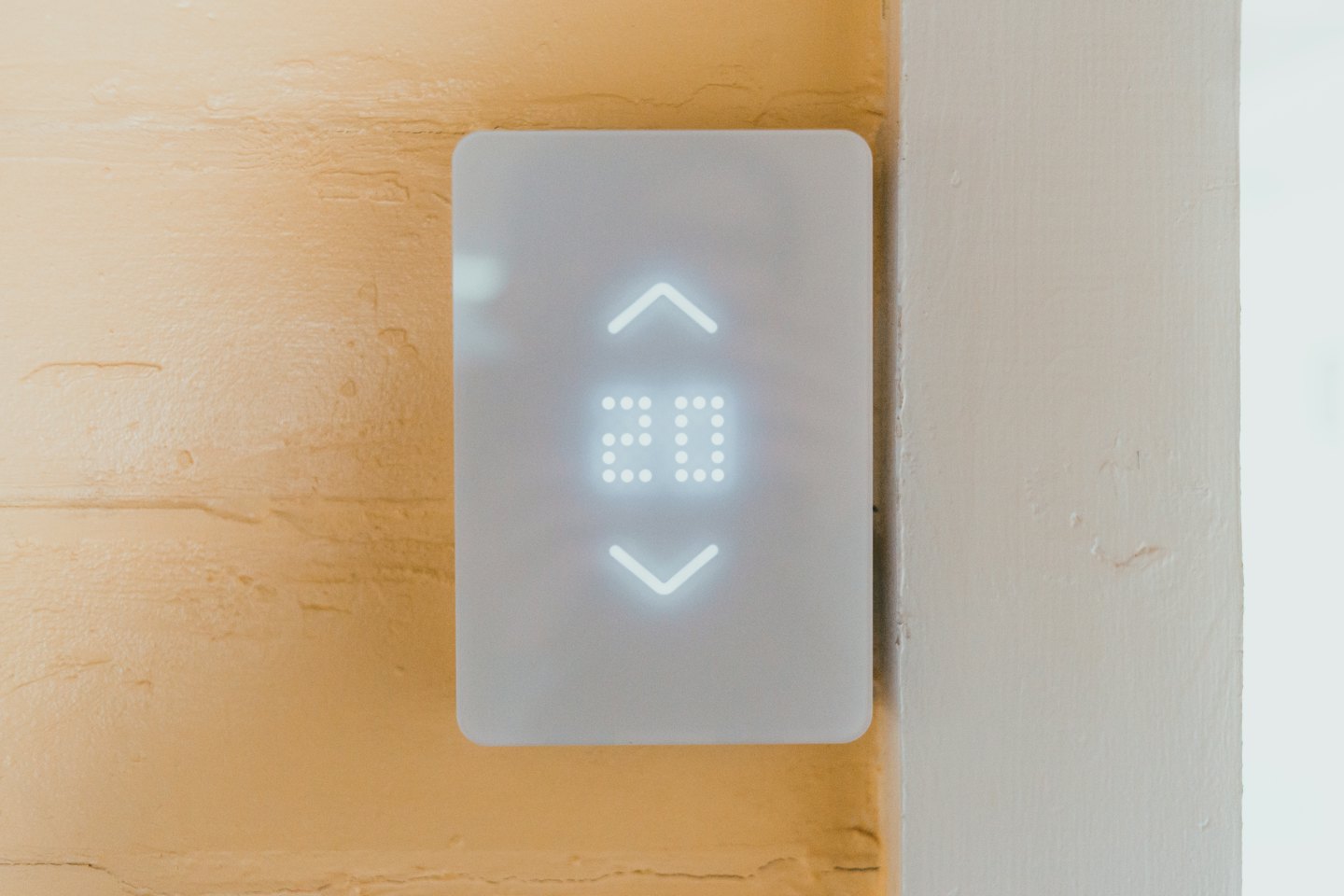 A white smart thermostat displays the number twenty on a wall.